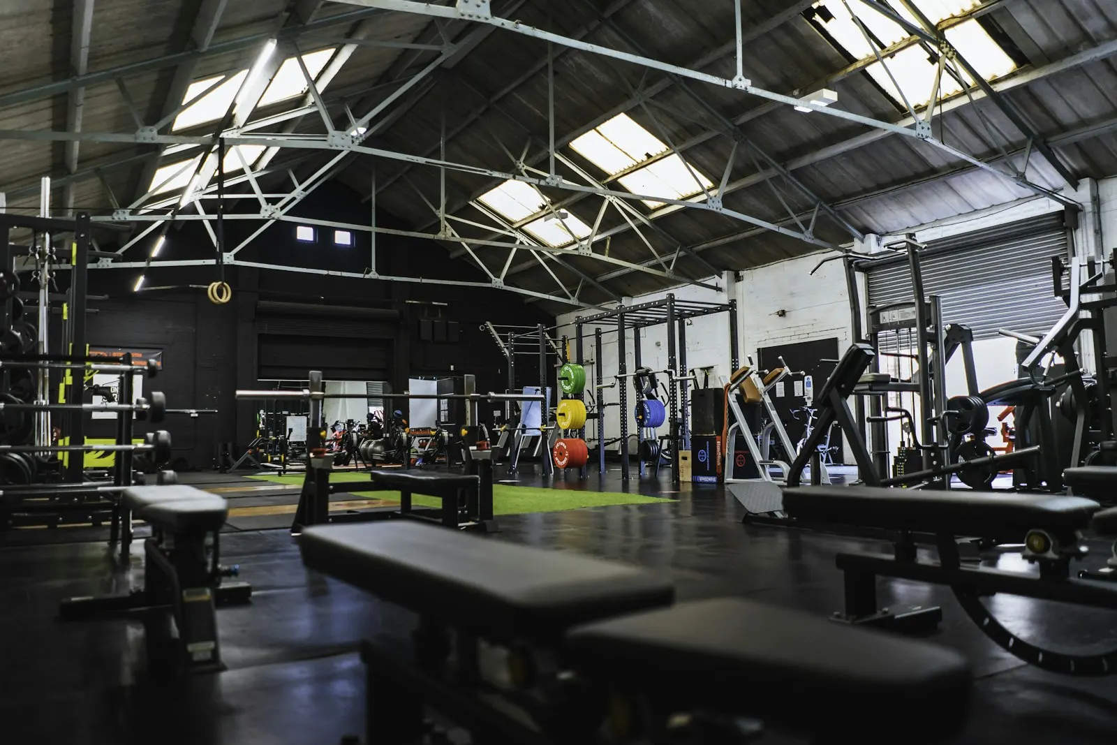 A wide training floor with benches, racks and a turf strip under skylights